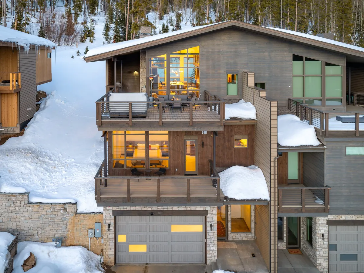 An inviting exterior view of the villa shows a balcony with seating, expansive windows, and a snowy roof, with touches of wood and stone for warmth. The scene suggests an ideal spot for family members to gather and relax together, bridging the private comforts of the villa with the surrounding mountain landscape.