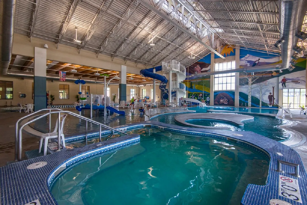 This vibrant interior image captures children gleefully playing on colorful water slides and splashing in the swimming pool, surrounded by cheerful murals. The scene bursts with energy and excitement, highlighting the family-friendly amenities and opportunities for fun that the Grand Park Rec Center offers.