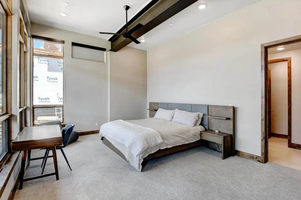 A tranquil, well-lit bedroom that includes a comfortable bed and a dedicated work desk by a window. The workspace is enhanced by natural light, making it ideal for focused work or study, and the room’s layout balances relaxation with productivity.