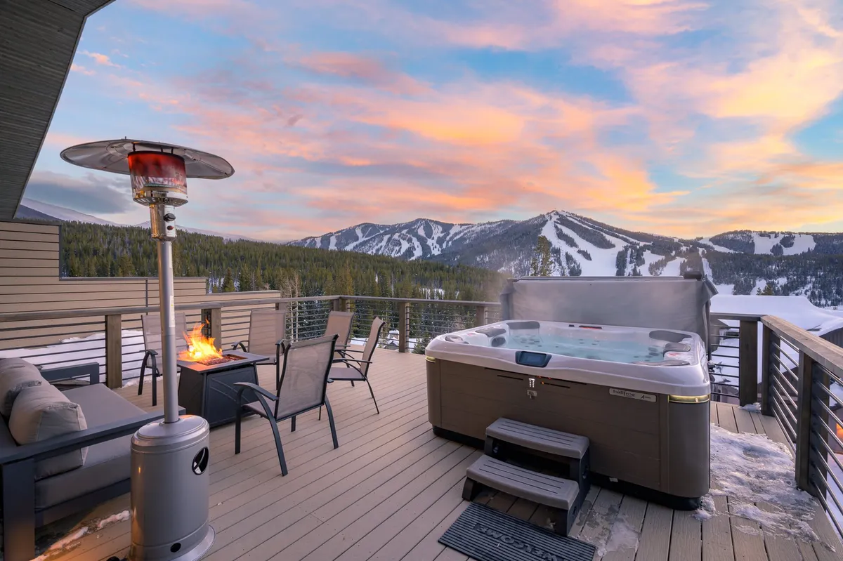 This image features an outdoor hot tub with a scenic mountain view, patio heater, and plush outdoor seating. The tranquil setting showcases the space as ideal for relaxing in the hot tub, enjoying the sunset, or gathering around the fire pit, with the deck amenities visible and inviting.