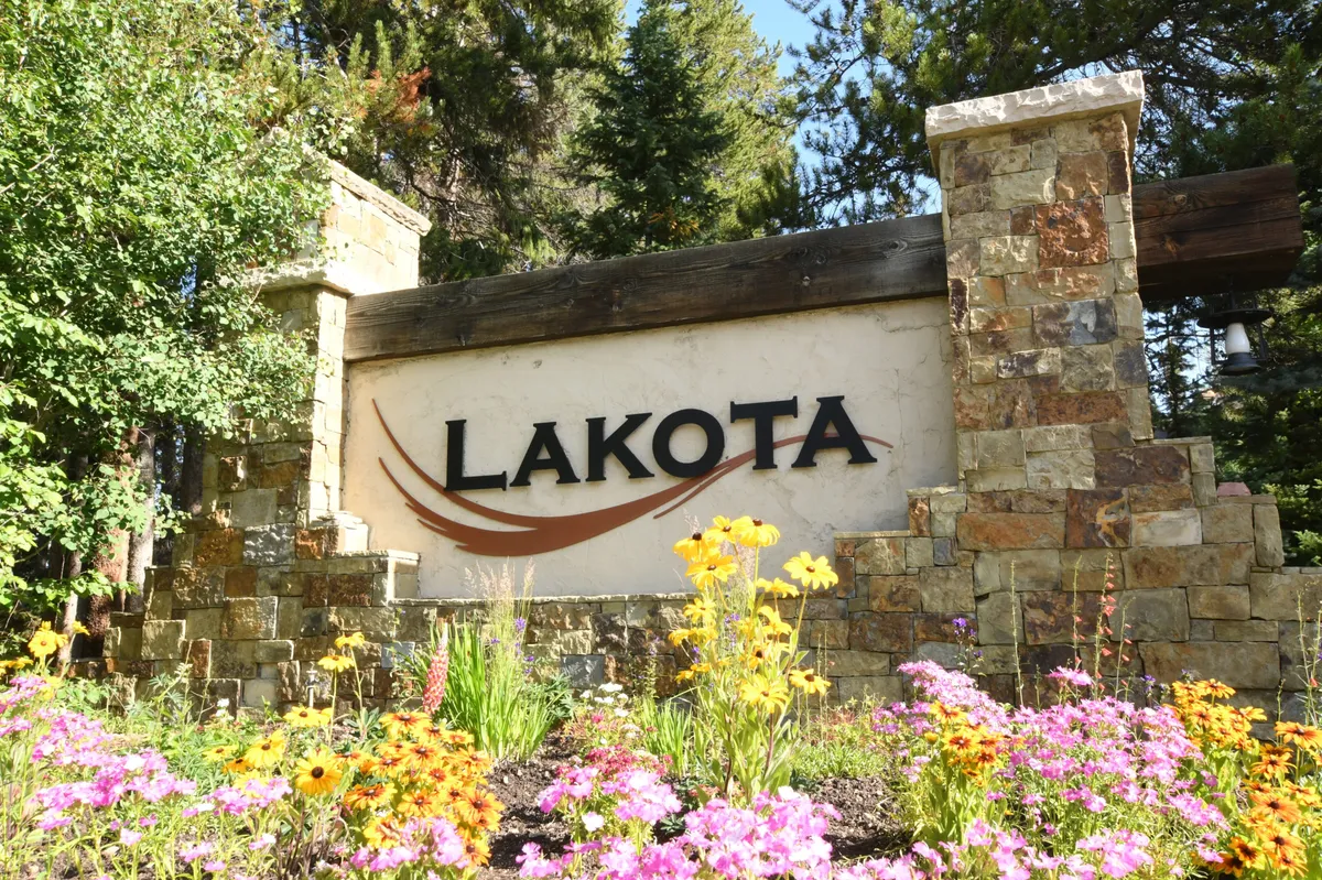 This exterior image features the LAKOTA sign set amidst vibrant flower beds and a sturdy stone structure. The surroundings are lush, inviting, and suggest a welcoming entrance to a scenic area, ideal for guests arriving for an adventure or a picturesque day trip.