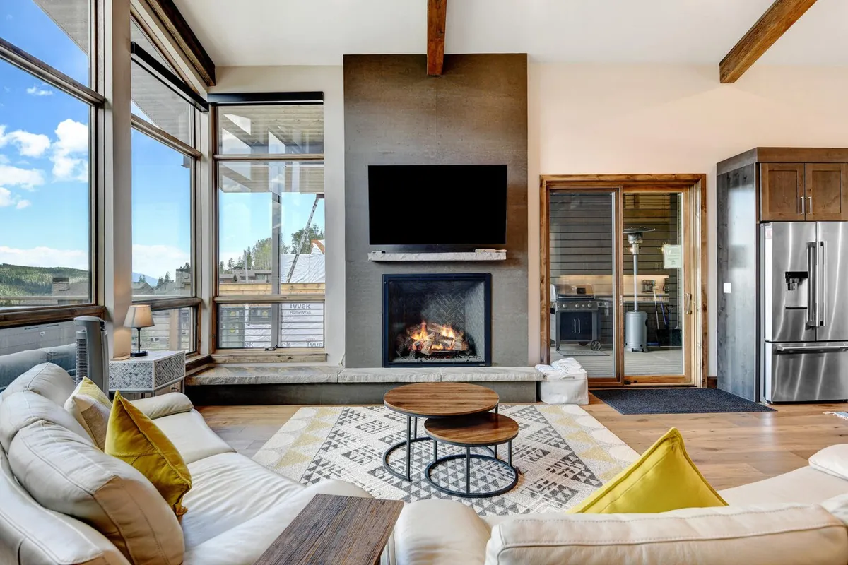 A comfortable, stylish living area with a large sofa, coffee table, modern fireplace, and expansive windows letting in natural light. The setting suggests a warm, relaxing environment perfect for unwinding after adventures, with a focus on comfort and high-end finishes.