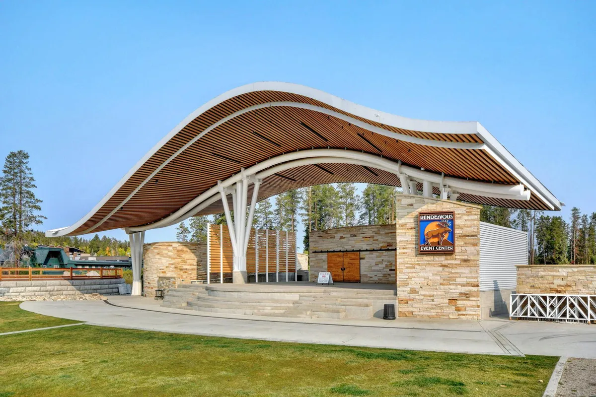 This exterior shot features the distinctive curved roof and stone walls of the Hideaway Park amphitheater, with its stage set for community events and concerts. The outdoor space looks welcoming and festive, inviting groups and families to gather for entertainment and bonding.